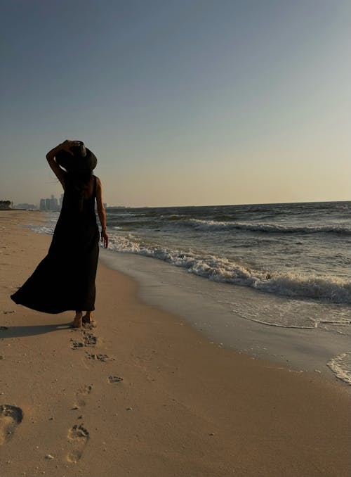 Woman in Dress and Hat Walking on Beach