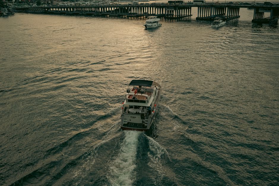 Drone shot of a yacht cruising through calm waters near a pier in the evening light.