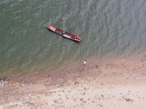 Free Aerial shot of a man beside a red boat on a sandy shoreline, capturing solitude. Stock Photo