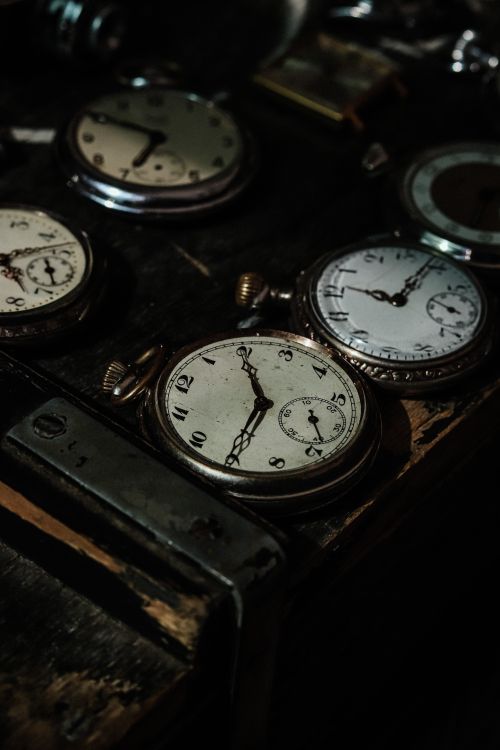 Free A collection of vintage pocket watches displayed on a dark wooden table in low light. Stock Photo