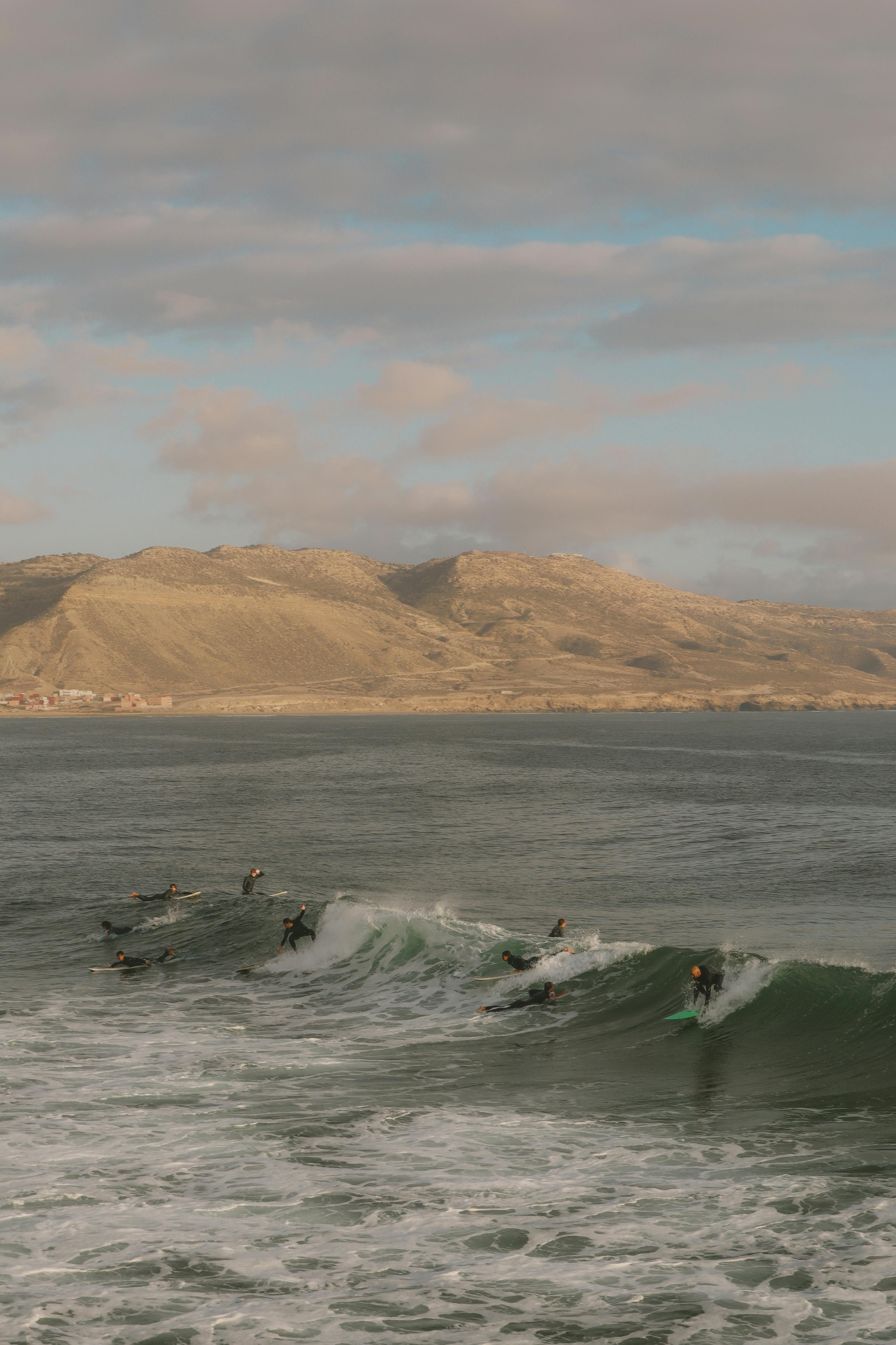 Surfers riding waves at Imsouane beach, Morocco under a bright sky.