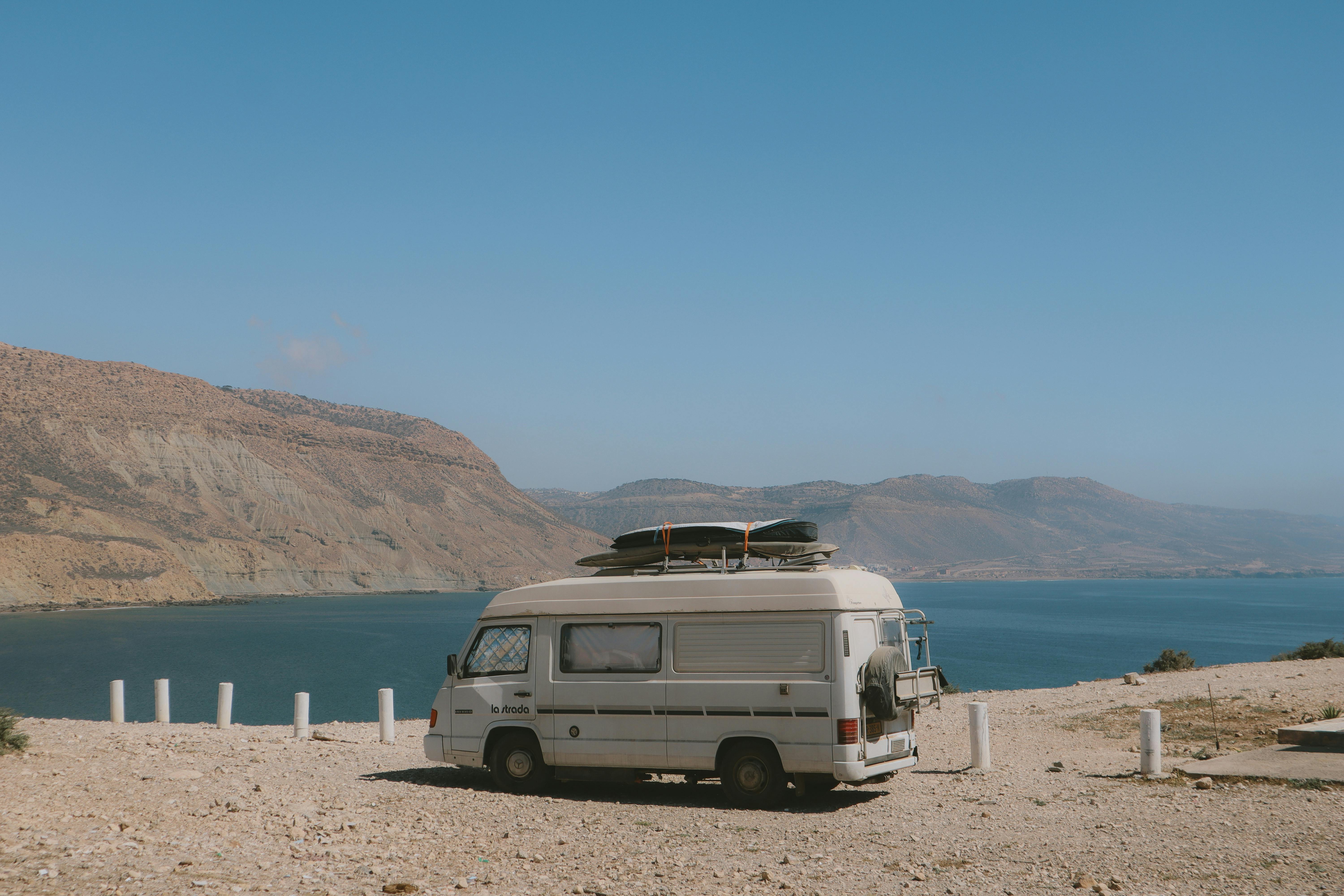 A camper van parked by the stunning lakeshore in Imsouane, Morocco, under a clear blue sky.