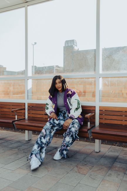 Stylish woman posing on a bench in urban setting, showcasing vibrant fashion trends.