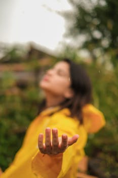 Blurred view of a woman in a yellow raincoat reaching out her hand outdoors.