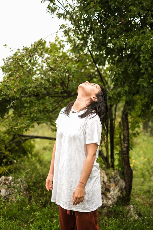 Free Woman in a white shirt standing amid lush greenery with head back. Natural forest ambiance. Stock Photo