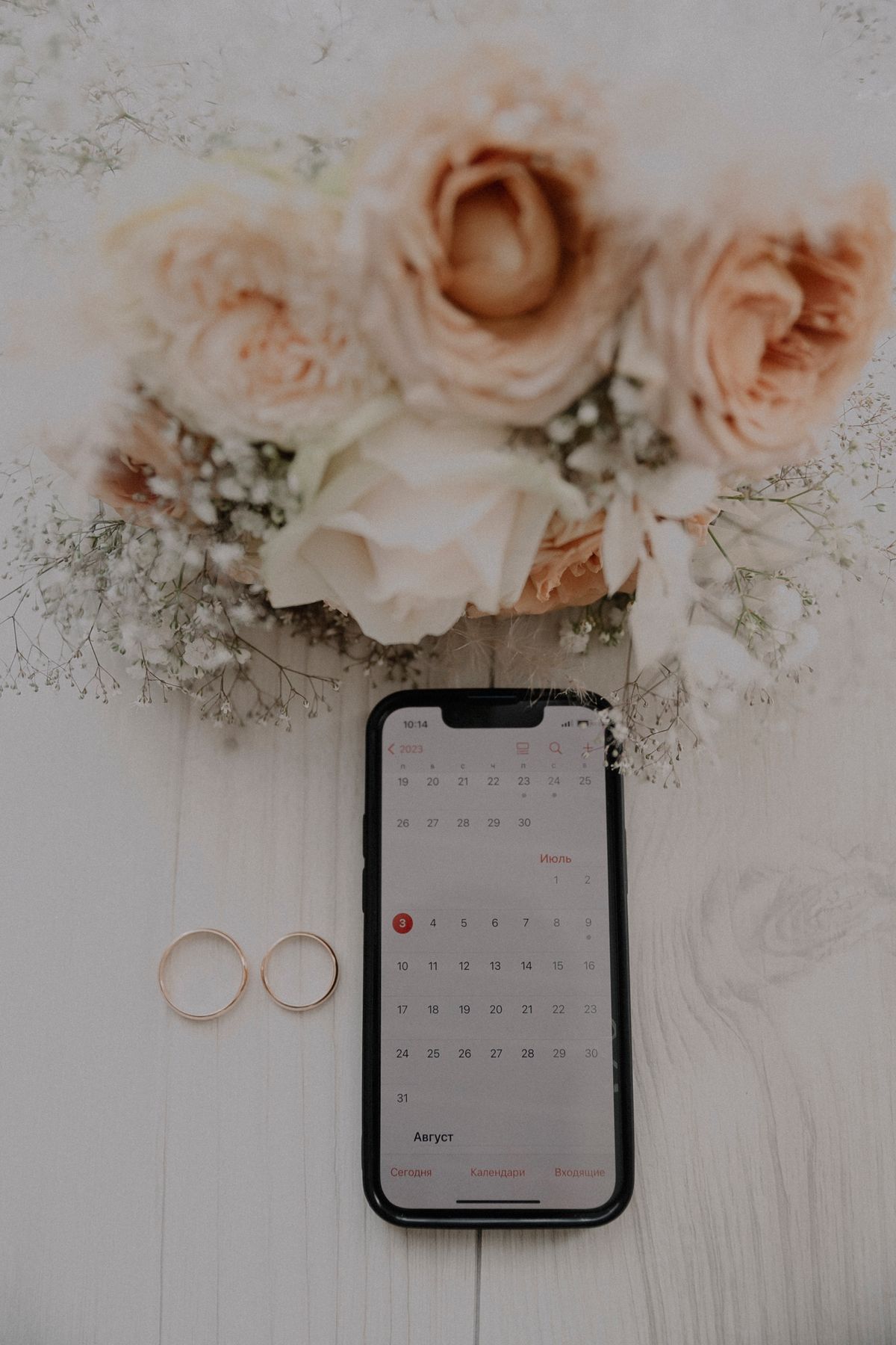 A wedding planning flatlay with flowers, rings, and a digital calendar display