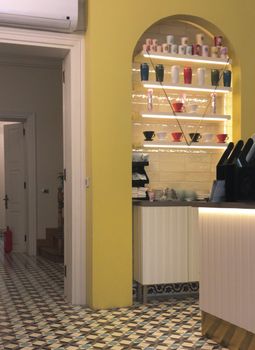 A cozy kitchen featuring yellow walls, arched shelves with colorful cups, and patterned flooring.