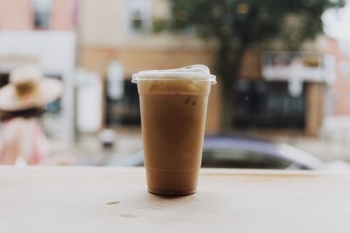 Free Iced coffee in a plastic cup on a table by a city street. Urban morning vibe. Stock Photo