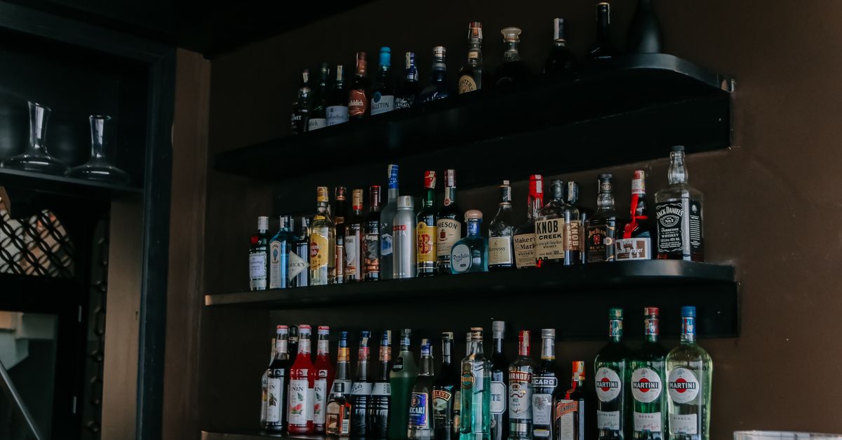 A modern bar with a wide selection of liquor bottles arranged on sleek black shelves.