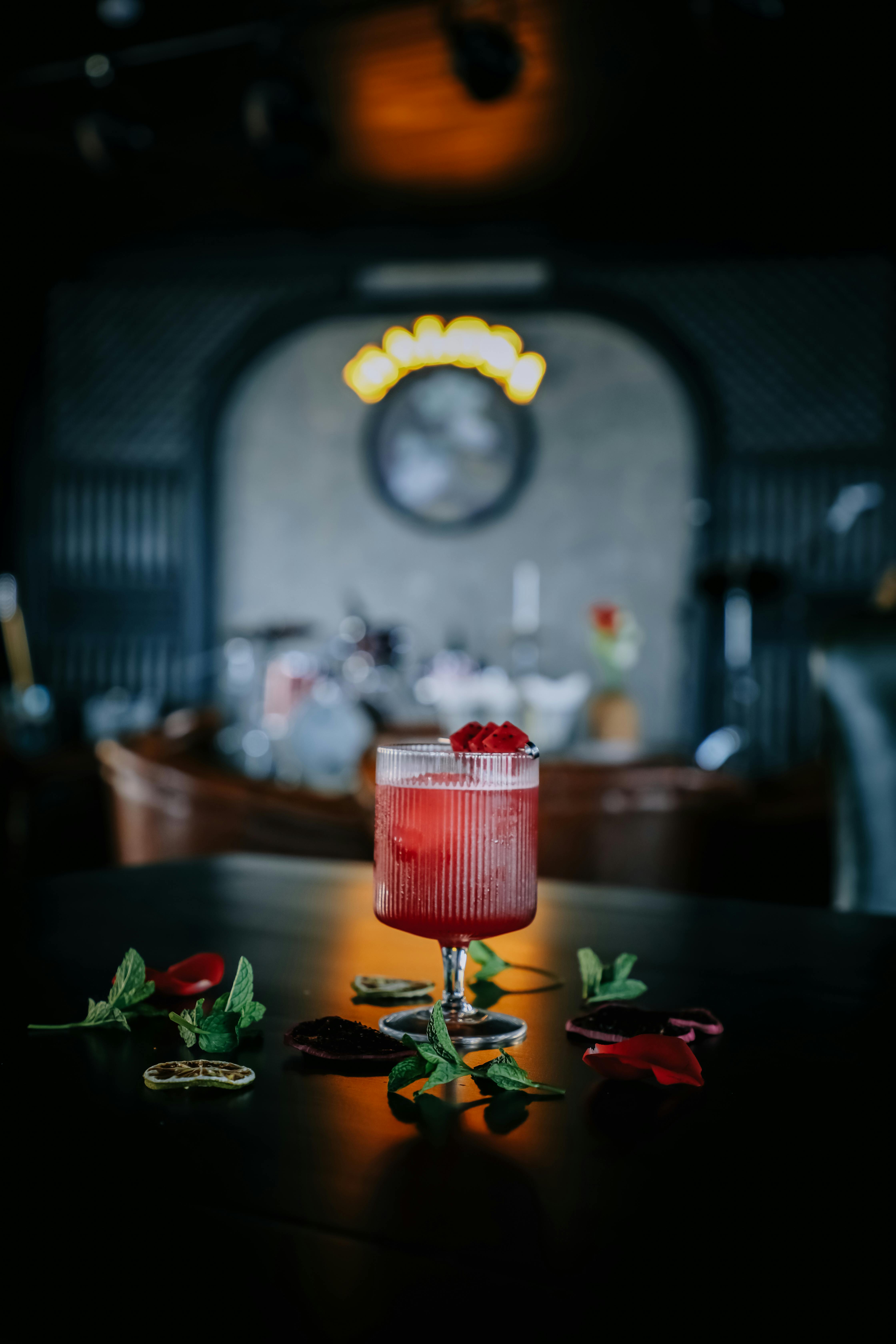 A vibrant red cocktail garnished with mint and petals in a stylish nightclub environment.