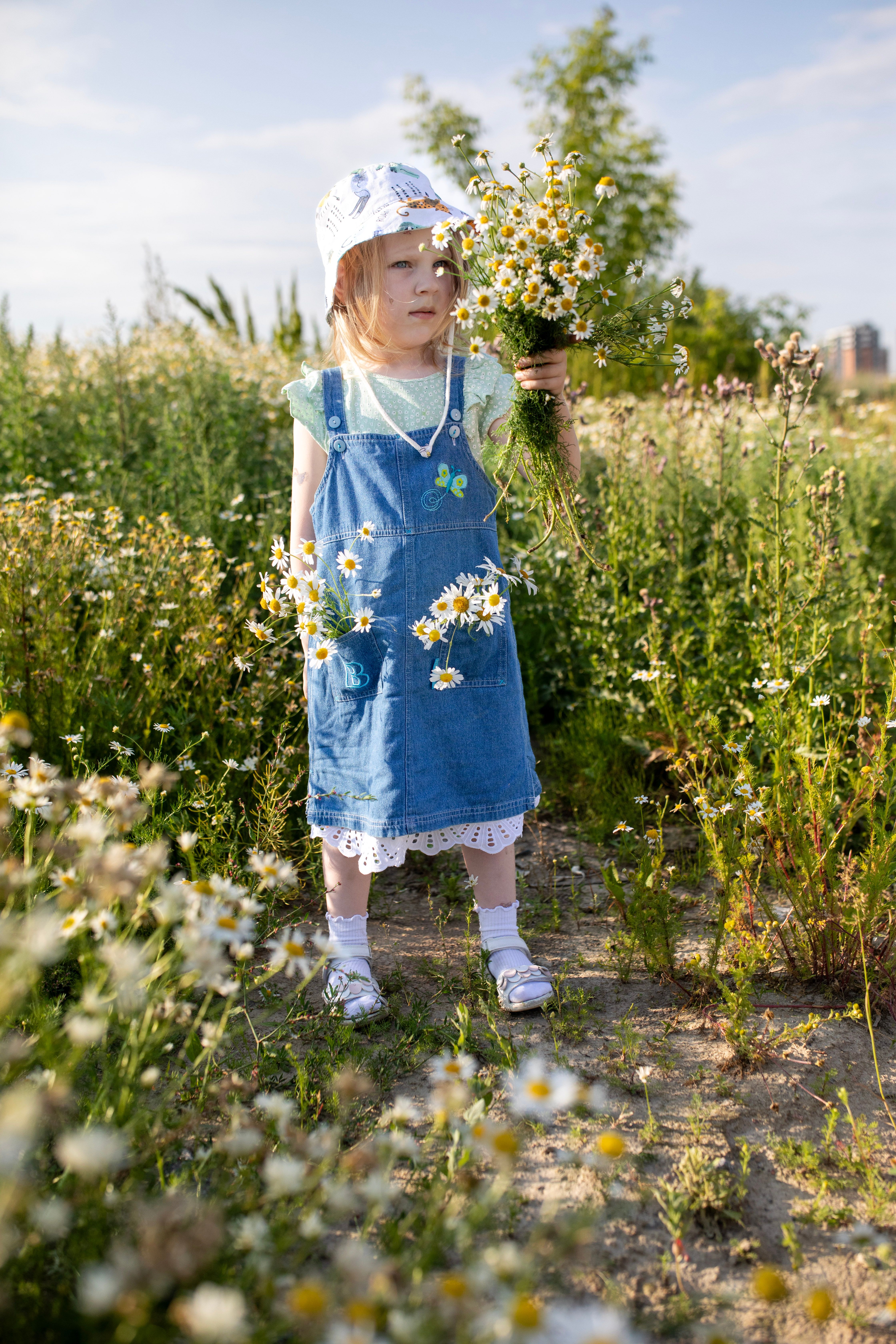 Little Girl in Denim Dress Holding Daisies in Hand  Free Stock Photo