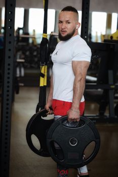 Strong man in a gym showing weightlifting strength with gym equipment background.