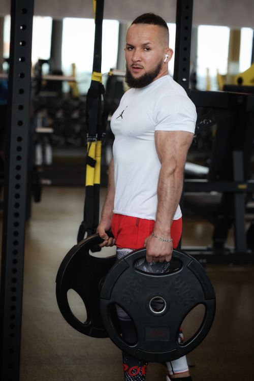 Free Strong man in a gym showing weightlifting strength with gym equipment background. Stock Photo
