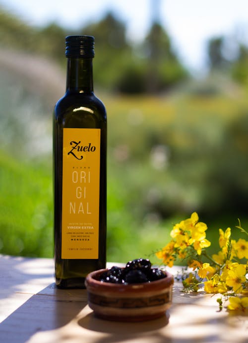 Close-up of a Bottle of Cooking Oil Standing on a Table next to Flowers and Fruit 