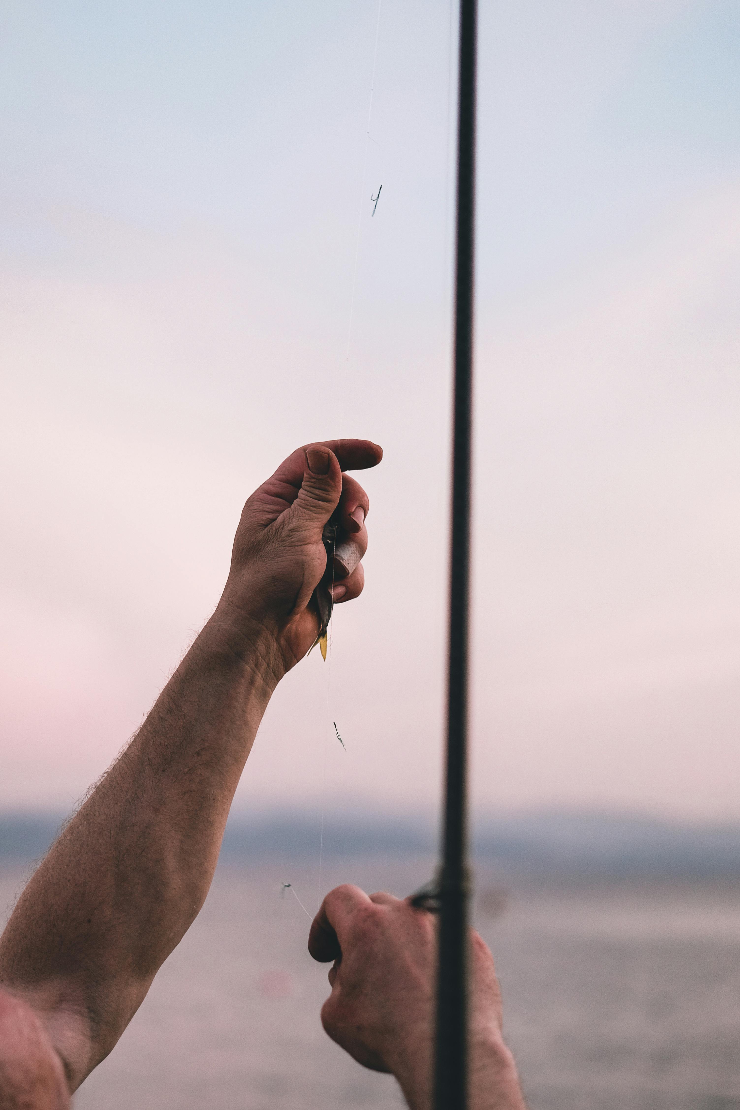 A serene close-up shot of a person preparing a fishing line by the sea during twilight.