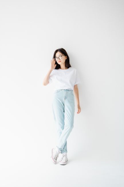 Woman in casual white tee and jeans posing in a bright studio with eyeglasses.