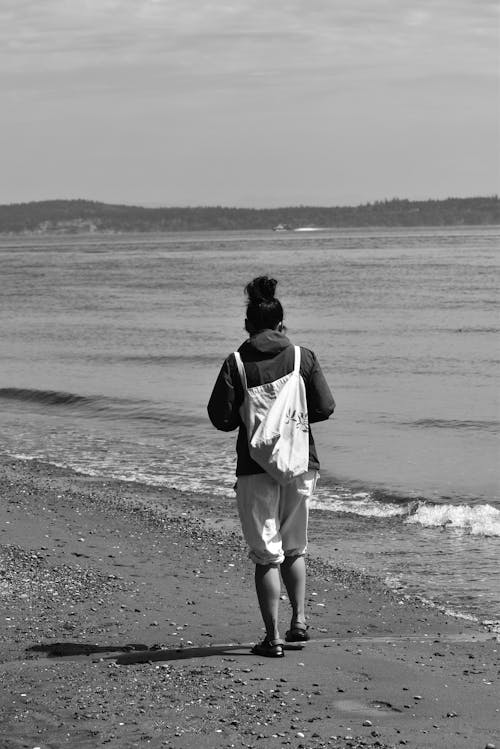 Brunette Woman with Bag on Back Walking Along Seashore