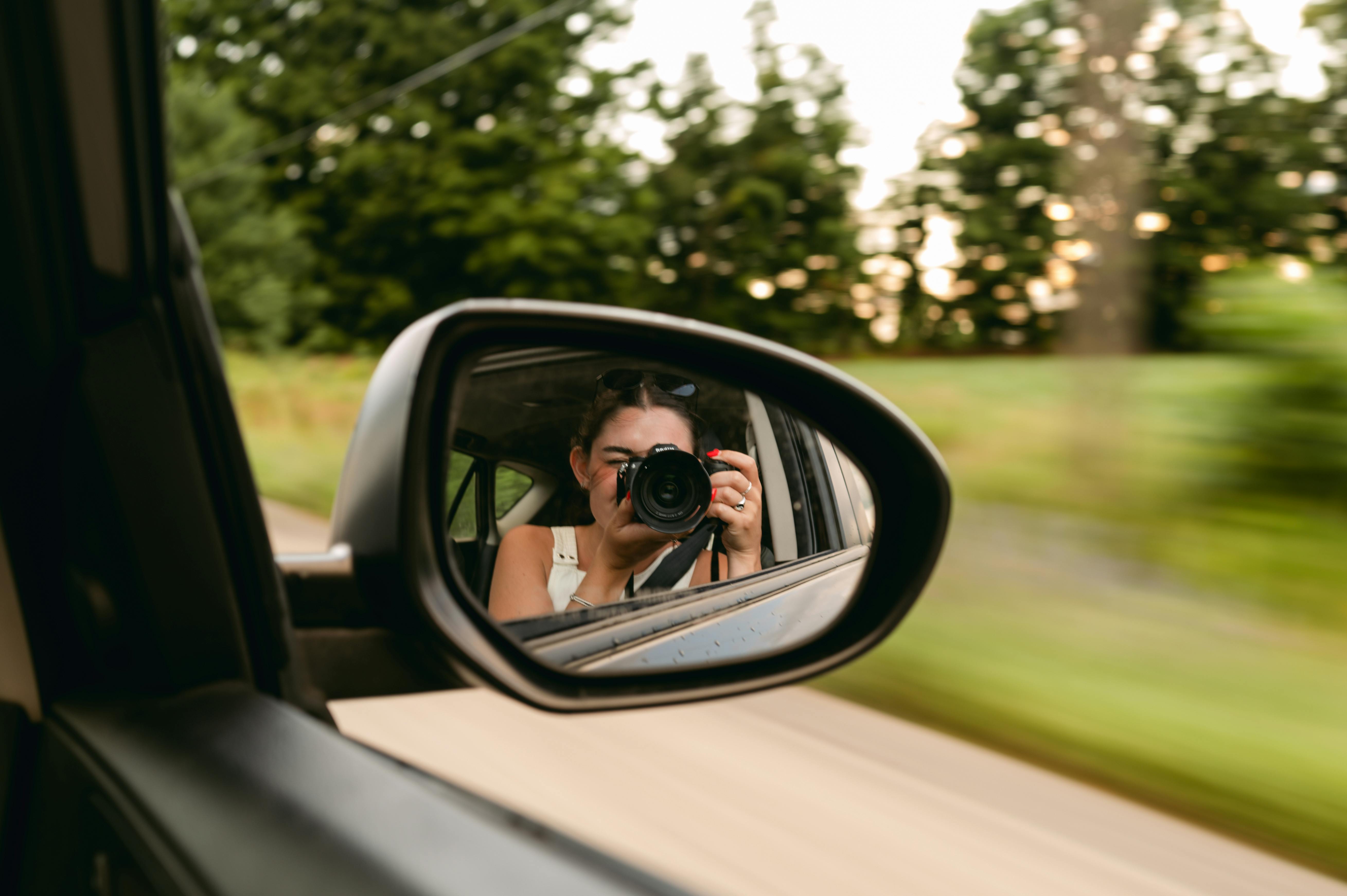 Free Photographer takes a picture from a car side mirror with blurred trees in the background. Stock Photo