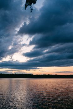 Peaceful lake scene at sunset with dramatic clouds reflecting on the water's surface.