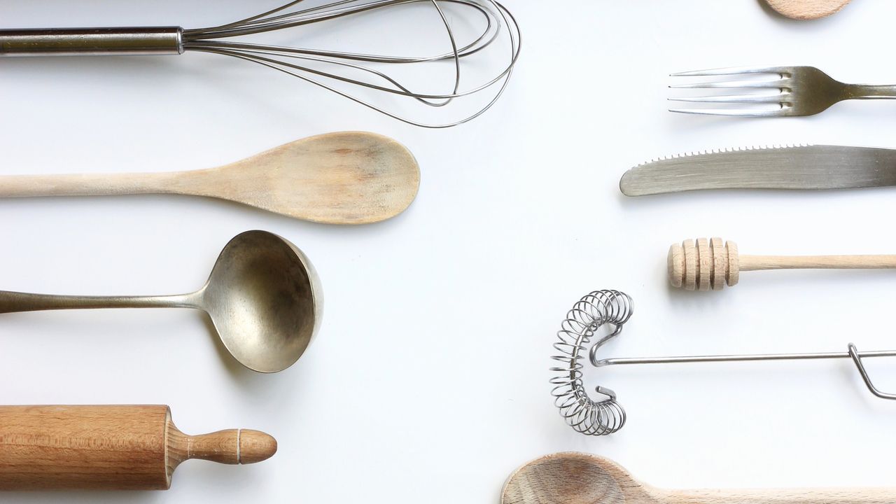 Wooden and metal kitchen utensils arranged on a pale background.