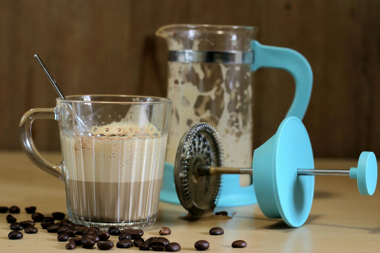 French press beside cup on table with scattered coffee beans