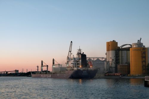 Free A beautiful sunset scene of a ship at Gdańsk harbor, highlighting industrial structures and calm waters. Stock Photo