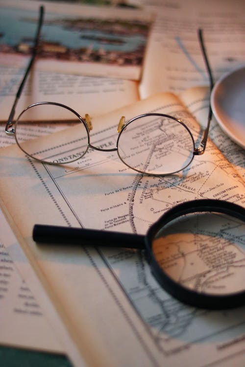 Eyeglasses and a Magnifying Glass Lying on a Vintage Book with a Map 