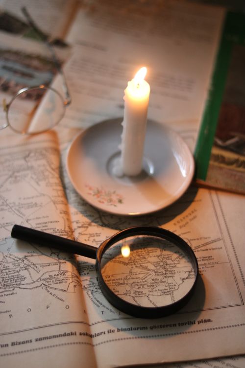 Free A vintage setup including a map, magnifying glass, candlelight, and eyeglasses, evoking exploration and mystery. Stock Photo