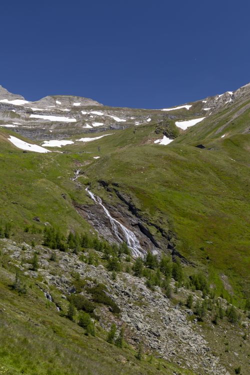 Free Beautiful view of an alpine mountainside with cascading waterfall under clear blue sky. Stock Photo