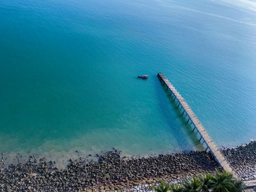 Free High angle view of a serene pier stretching into the calm blue sea with rocky shore. Stock Photo
