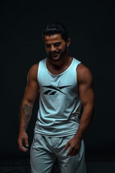 Portrait of a smiling man wearing a tank top showing his tattoos against a dark background.