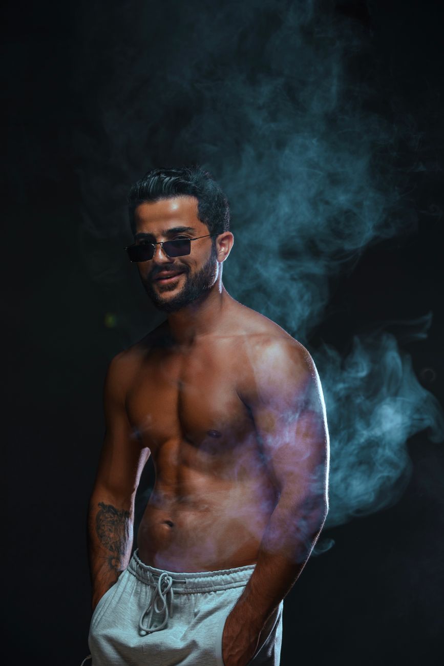 Portrait of a muscular man wearing sunglasses, enveloped in smoke. Moody lighting.