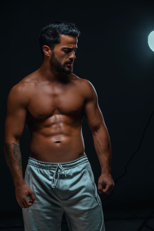 Free Shirtless muscular man posing against a black background in a professional studio setting. Stock Photo