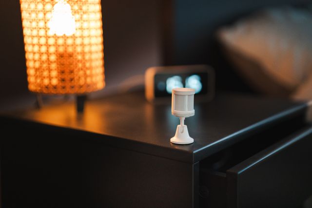 Stylish bedroom with smart motion sensor, lamp, and alarm clock on wooden nightstand. Related image for Smart Hotels: Key Lessons for Owners and Operators.