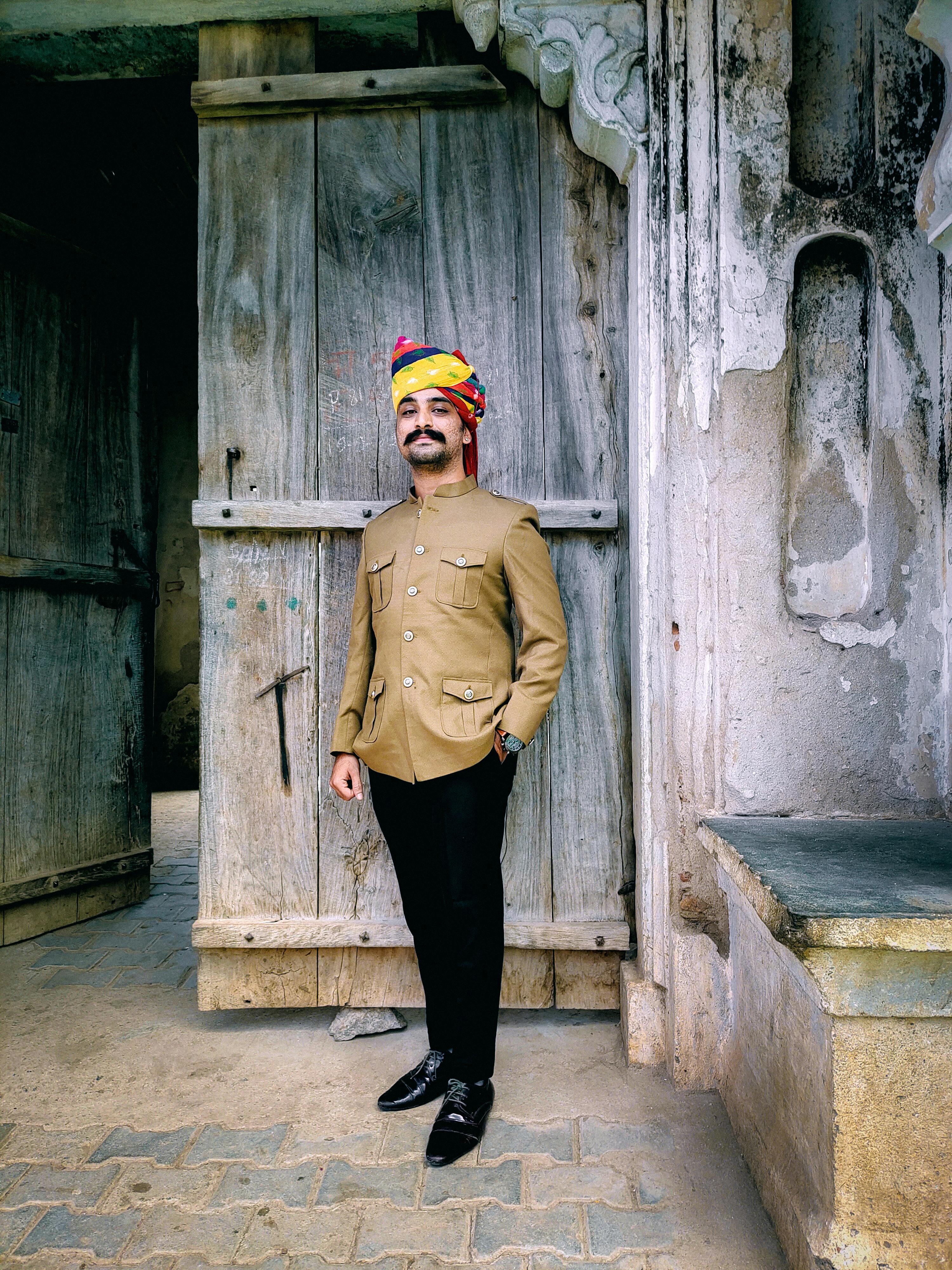 Man in traditional clothing with turban at entrance of historic building, exuding cultural charm.
