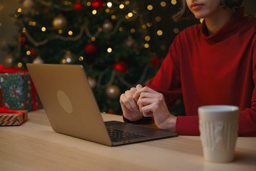 Woman Sitting at a Table and Using a Laptop on the Background of a Christmas Tree