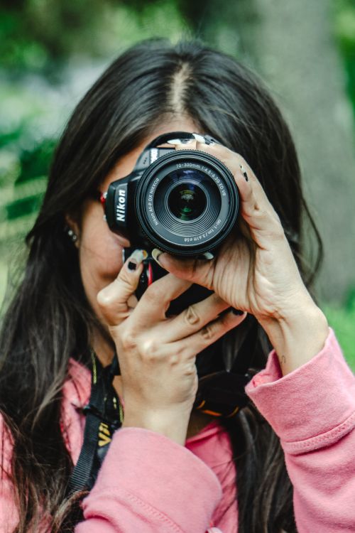 Free Portrait of a young woman taking a photograph in an outdoor park with greenery. Stock Photo