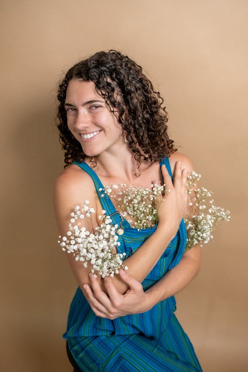 Studio Shot of a Young Woman Posing with Flowers Stuck behind Her Clothes 