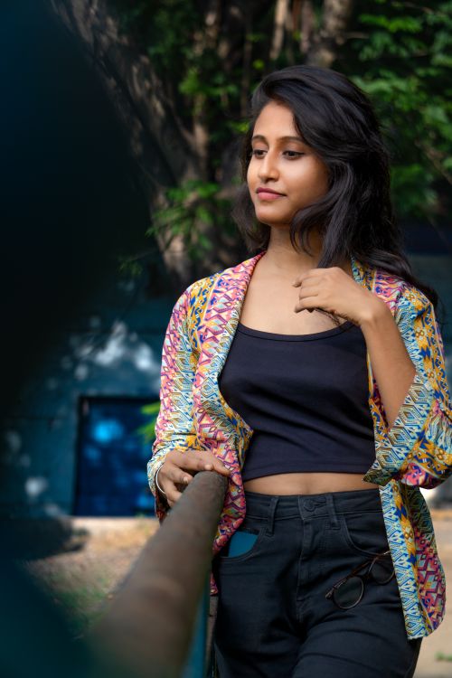 Free A young woman with long hair stands gracefully outdoors in a bright, colorful jacket. Stock Photo