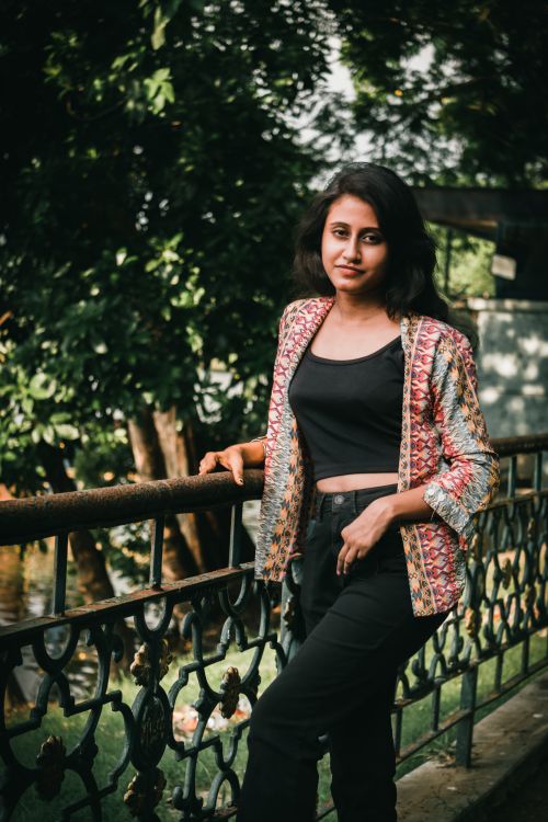 Free Portrait of a fashionable woman posing by a railing in a lush urban park. Stock Photo