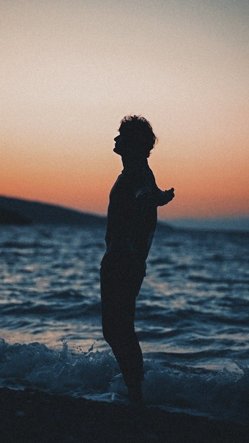 Silhouette of a Man Standing with Arms Spread on the Beach at Sunset 