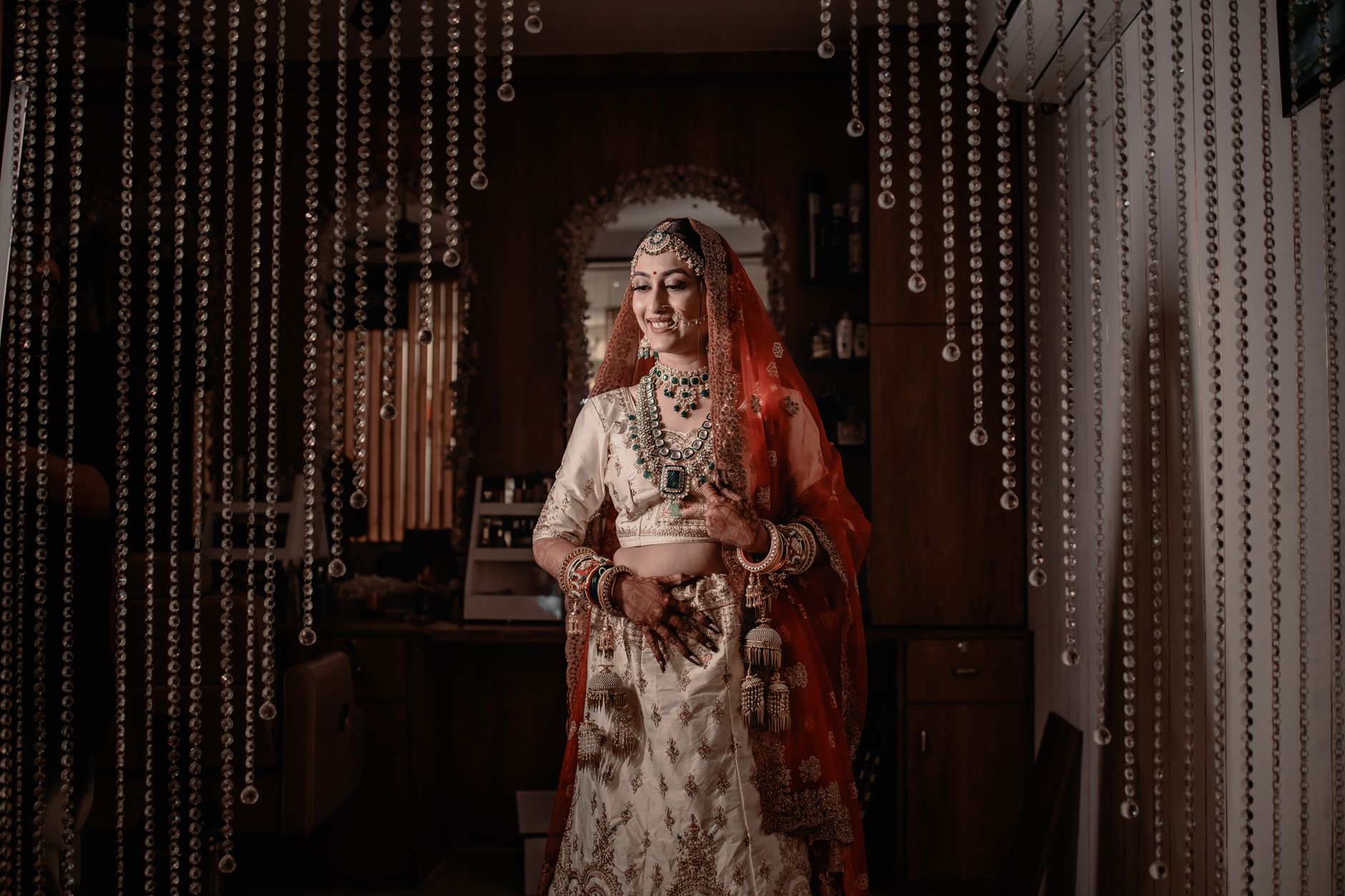 Beautiful Indian bride in traditional attire posing indoors with intricate jewelry and a joyful smile.