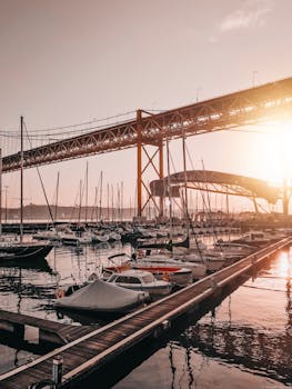 日落时分，宁静的码头边，船只停在一座引人注目的红桥下