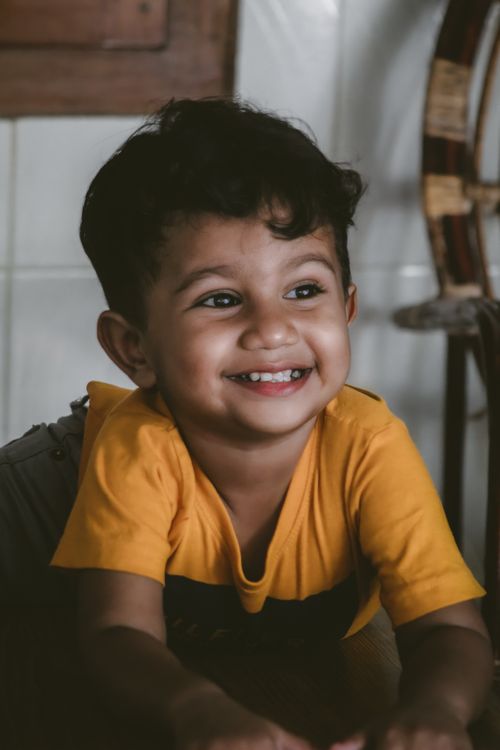 Free Adorable child with a big smile wearing a yellow shirt indoors. Stock Photo