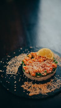 Elegant salmon tartare with lemon and sesame on a dark slate plate.