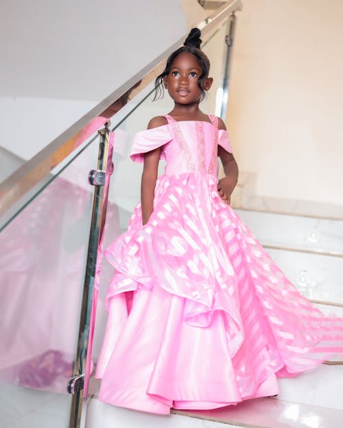 A Little Girl in a Pink Dress Standing on the Staircase 