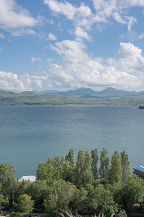 Free Peaceful landscape of a lake with distant mountains and lush trees under a clear blue sky. Stock Photo