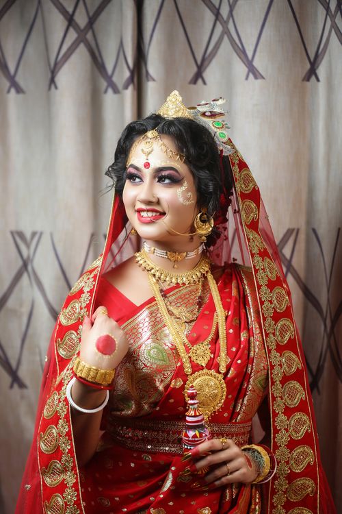 Free A South Asian bride smiling in traditional red and gold attire with intricate jewelry. Stock Photo