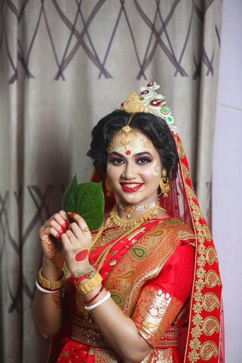 Free Elegant Bangladeshi bride in red traditional sari holding a leaf, adorned with jewelry. Stock Photo