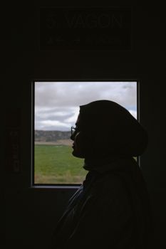 A silhouette of a woman wearing a headscarf on a train in Eskişehir, Türkiye, showcasing cultural travel.